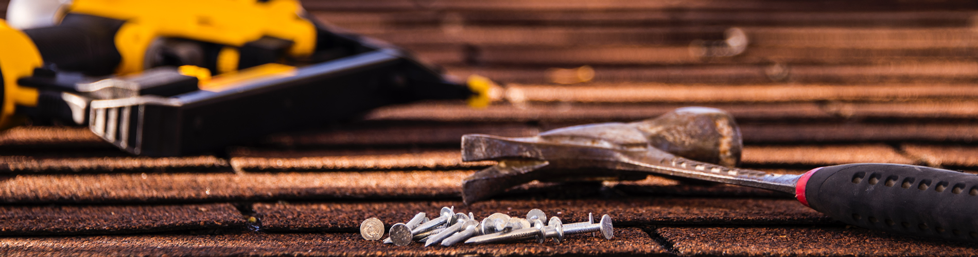 Close up shot of a residential roof with a hammer, nails, and nail gun on top